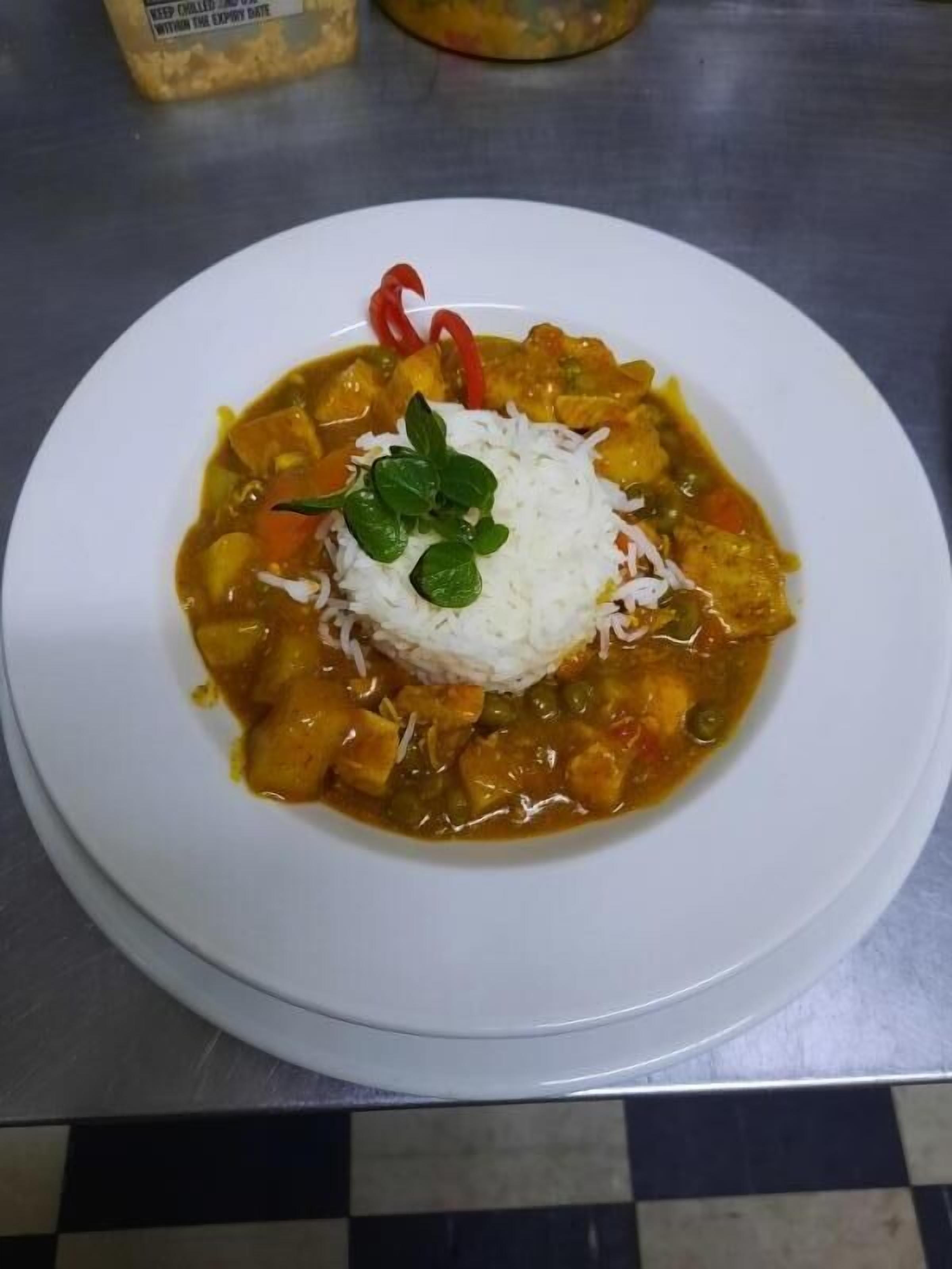 Une assiette de curry accompagnée de riz et de quelques garnitures, le tout servi dans une assiette blanche.