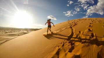 Una persona corriendo sobre una duna de arena, con cielo despejado y sol al fondo.