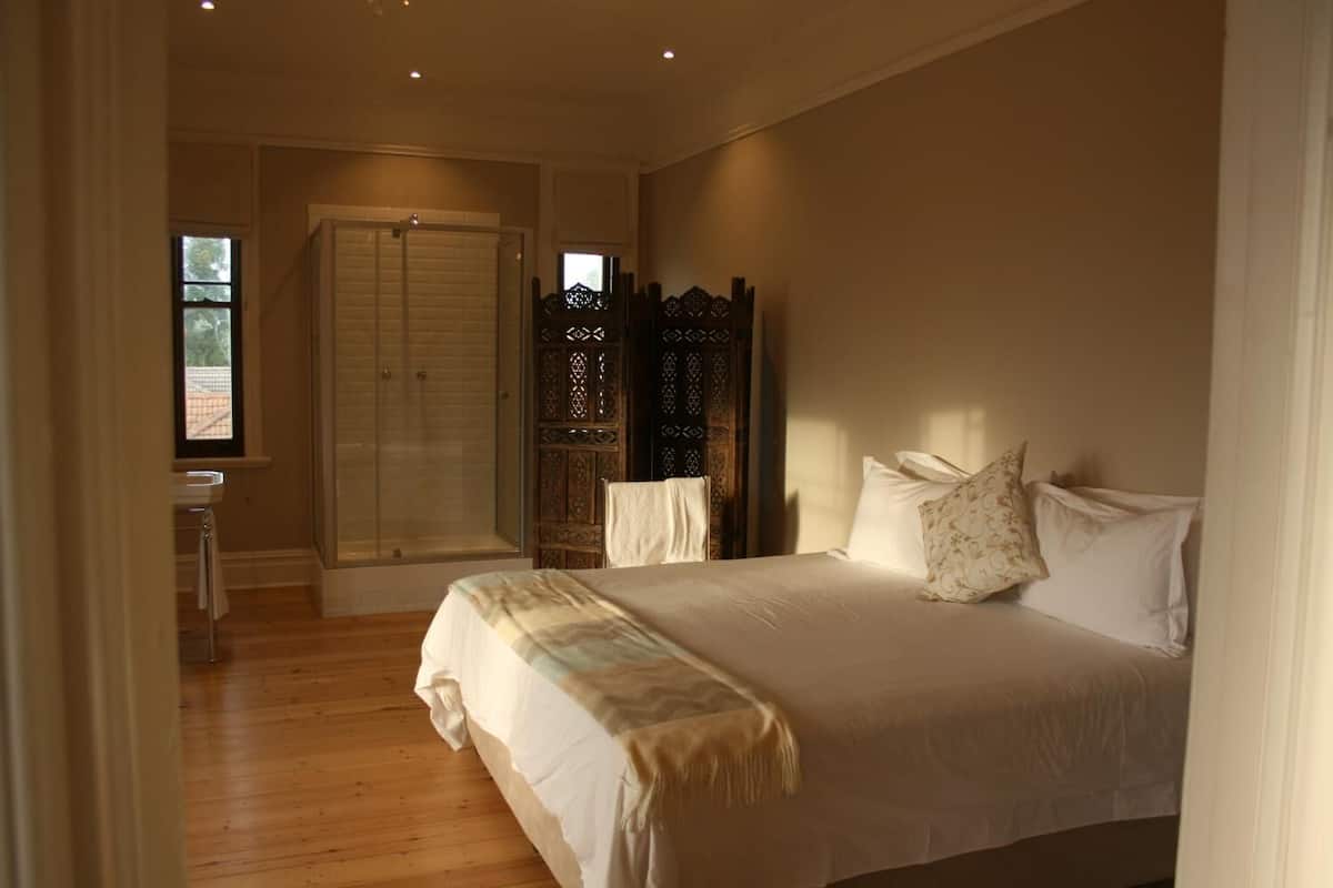 Un dormitorio con una cama grande, un armario de madera, un ventanal y un baño con lavamanos.