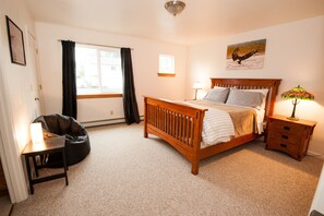 A bedroom with a wooden bed, a bedside table with a lamp, a chair, and a window with curtains.