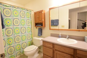 A bathroom with a patterned shower curtain, a toilet, a sink, wooden cabinets, and a mirror.