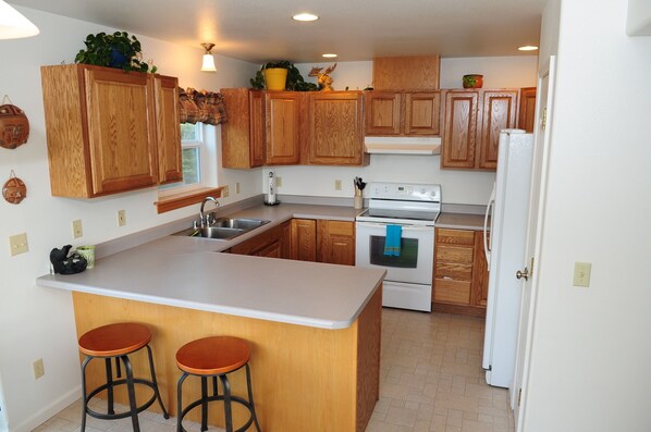 A kitchen with wooden cabinets, a white countertop, a stove, and two stools.