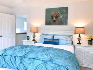 Une chambre à coucher avec un grand lit, deux tables de chevet avec des lampes, un tableau accroché au mur et une porte blanche.
