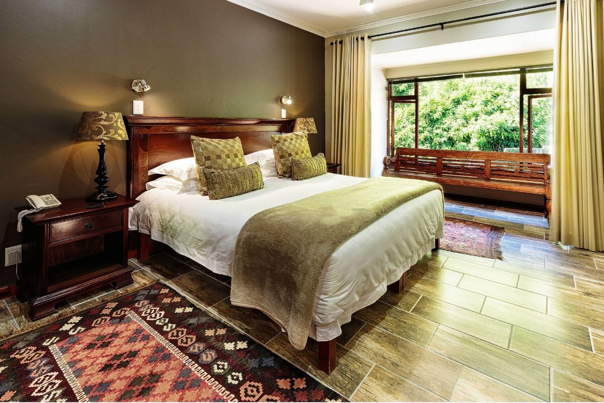 A neatly made bed with a wooden headboard, a bedside table with a lamp, and a patterned rug on the floor.