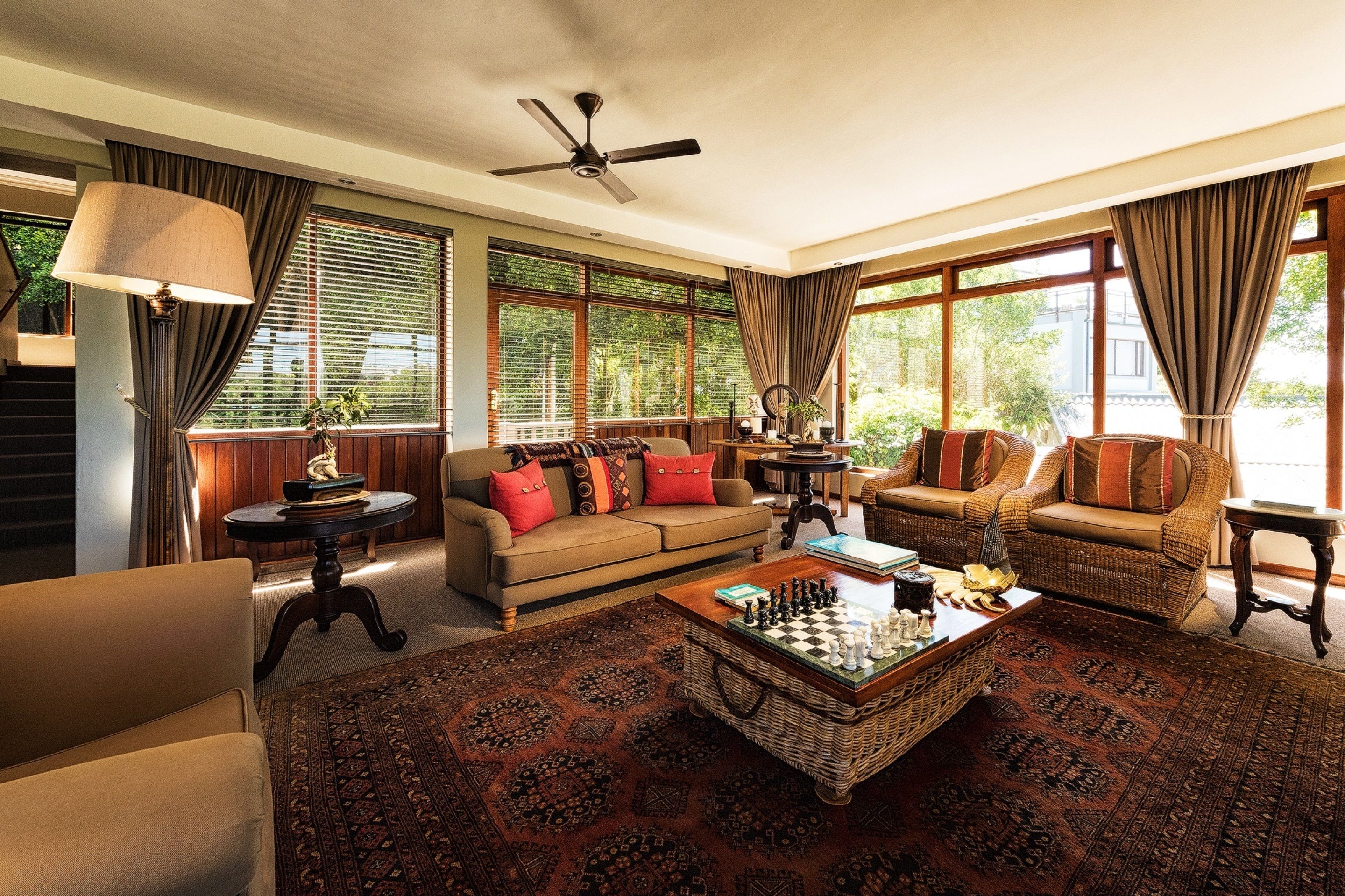 A spacious living room with a large window, a ceiling fan, and a chessboard on a central coffee table.