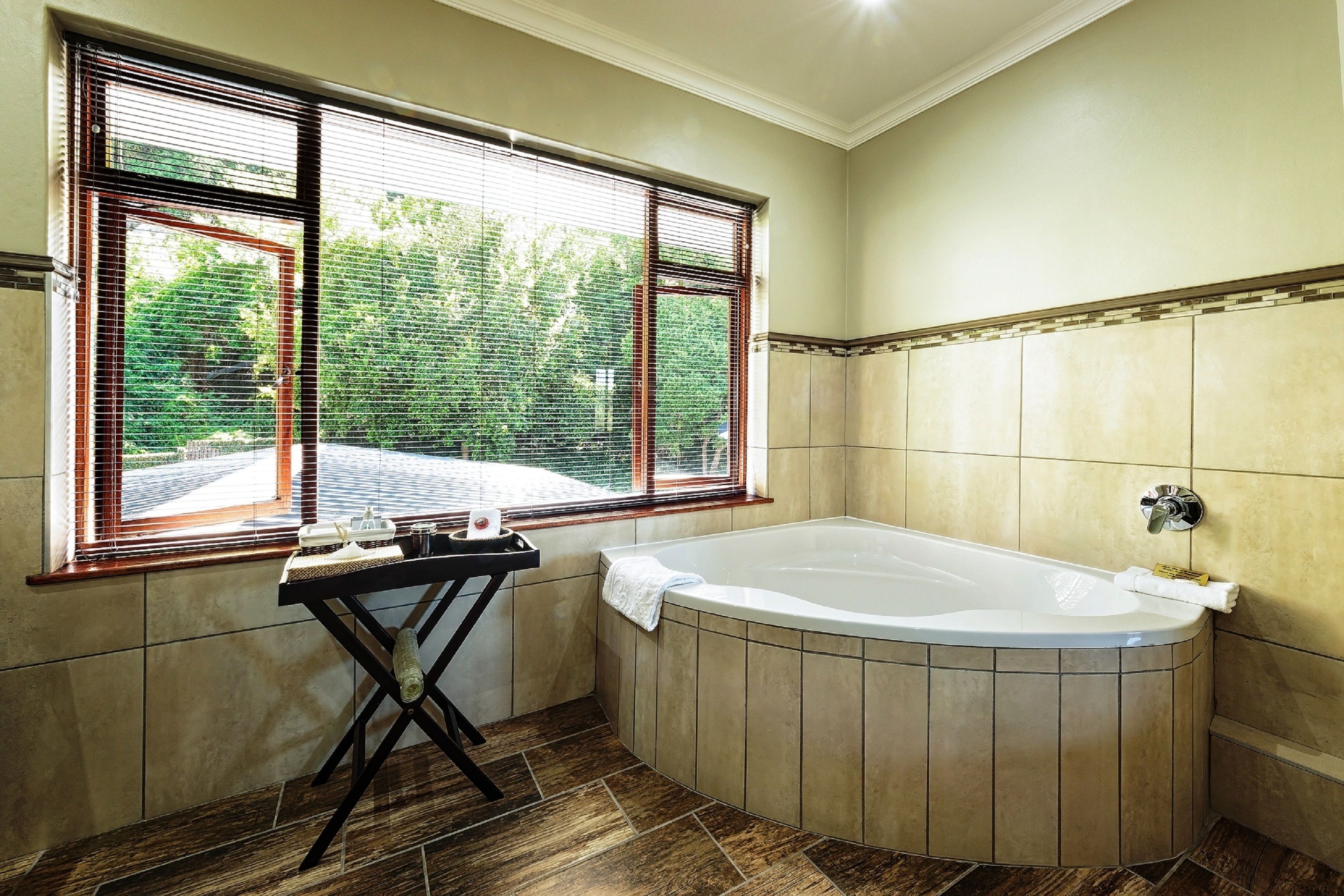 A bathroom with a large bathtub, a window with blinds, and a towel rack.