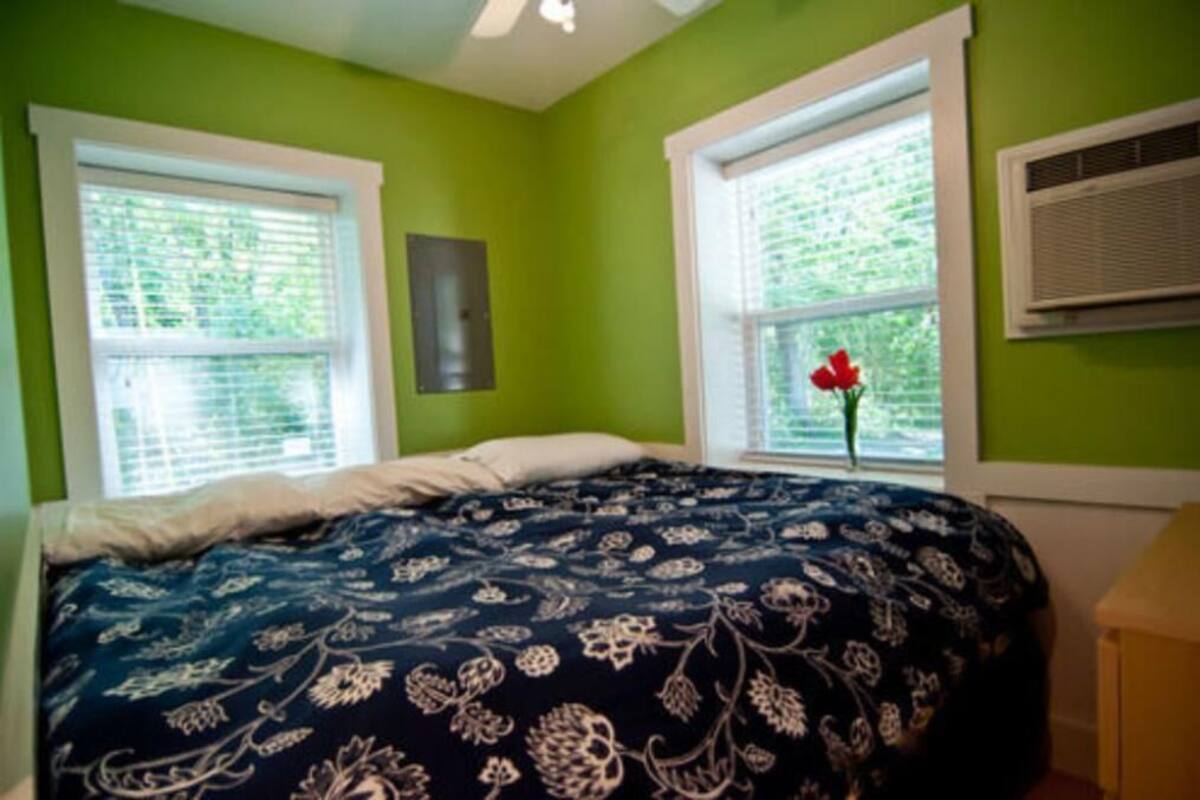 Ein Schlafzimmer mit einem Bett, zwei Fenstern und einer Wand-Klimaanlage.