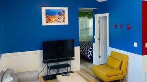 A living room with a flat-screen TV, a sofa, a yellow armchair, and a coffee table. - Blue Door Cottages (Monticello)
