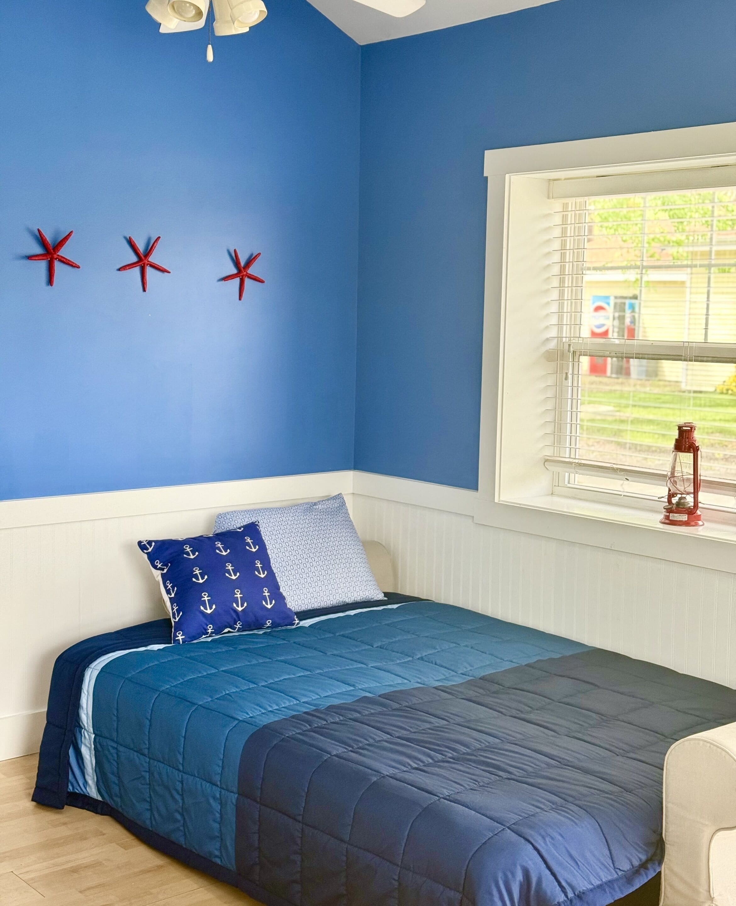 A bedroom with a bed, a window with blinds, and three red starfish decorations on the wall.