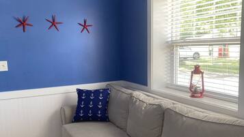 Een kamer met een blauwe muur, een beige bank en een raam met zonwering.