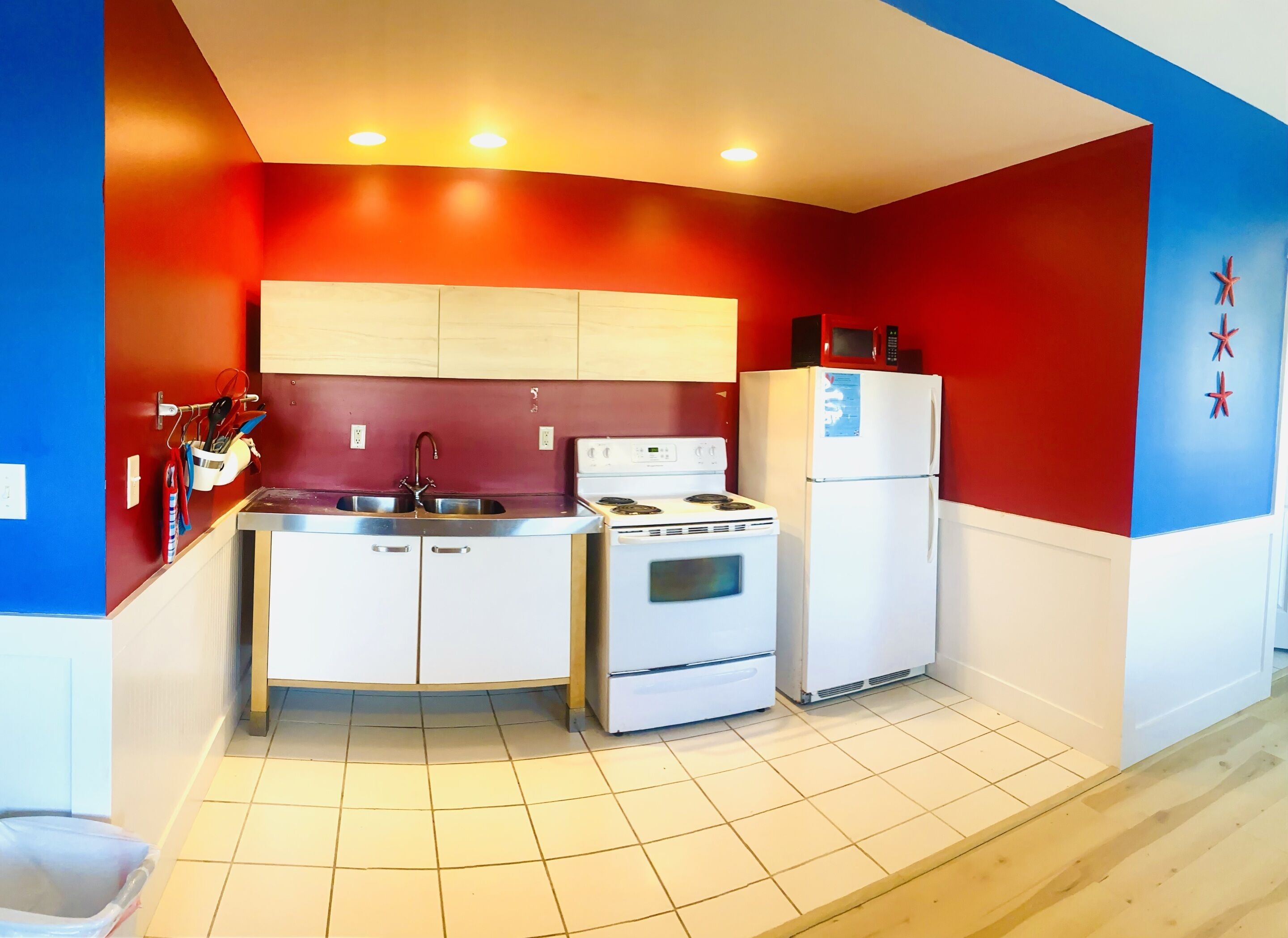 A compact kitchen with a sink, stove, and refrigerator, featuring red and white walls and a tiled floor.