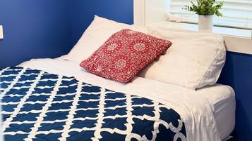 A bed with a blue and white patterned bedspread, a red floral pillow, and white pillows.