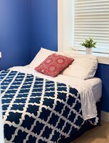 A bed with a blue and white patterned bedspread, a red floral pillow, and white pillows.