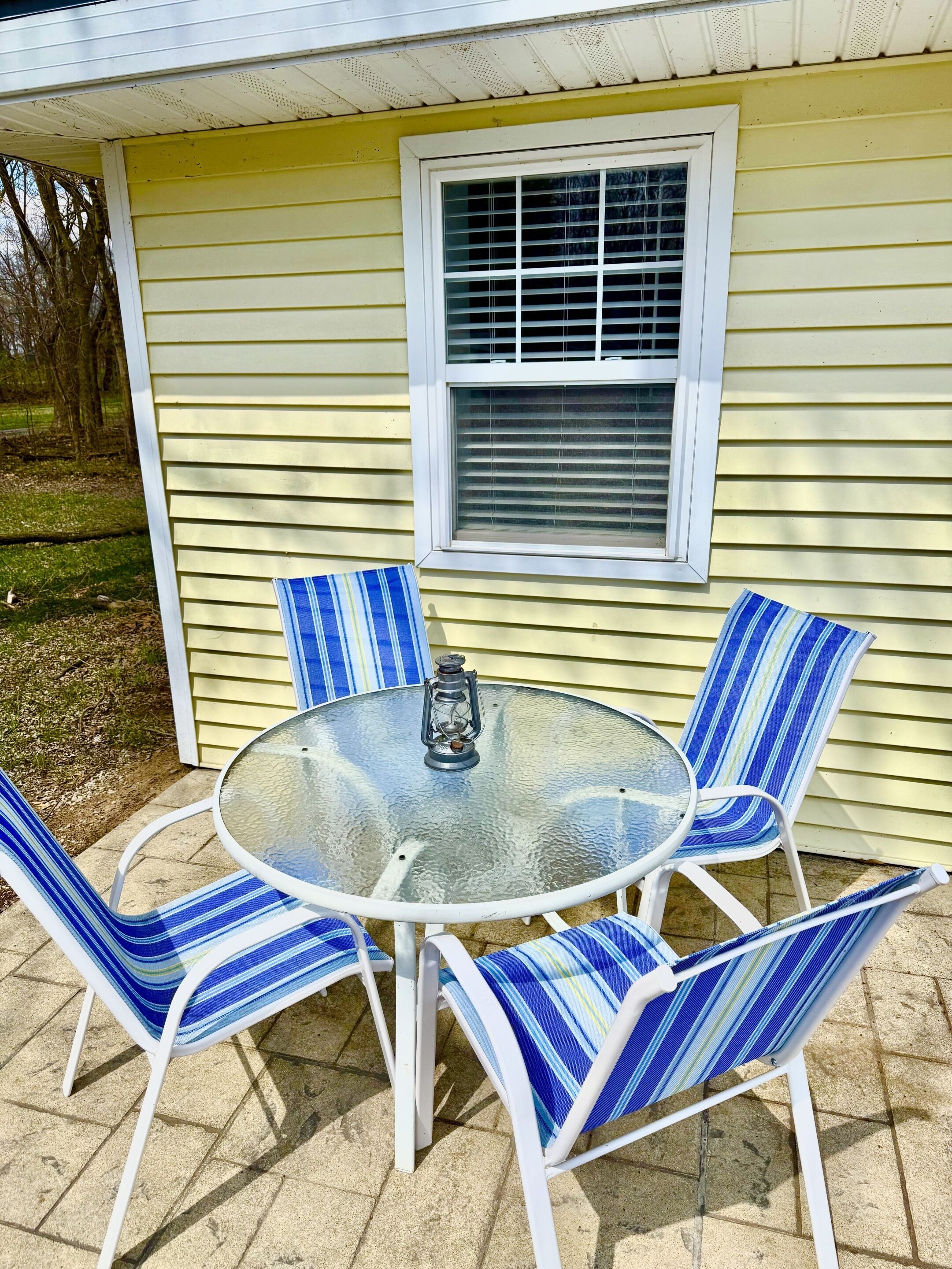 Une terrasse avec une table ronde en verre et quatre chaises à rayures.