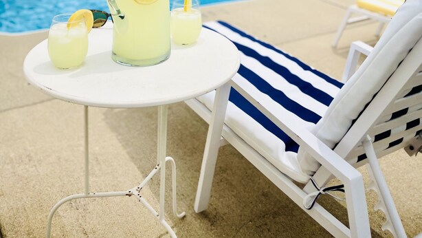 A poolside setting with a table and lounge chairs, a pitcher of lemonade, and a glass of lemonade. - Blue Door Cottages (Monticello)