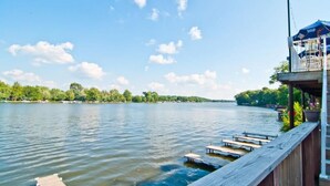 A lakeside view with a wooden dock extending into the water, a covered seating area with a blue canopy, and a distant shoreline with trees. - Blue Door Cottages (Monticello)