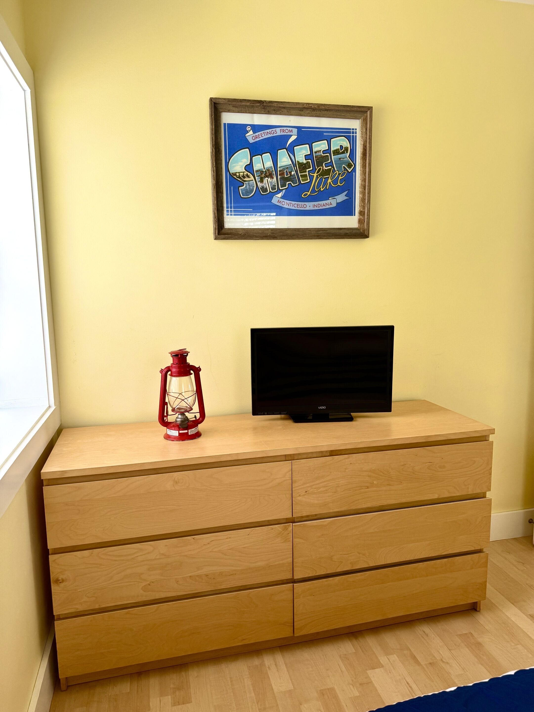 A wooden dresser with a television on top, a framed sign above it, and a red lantern beside the TV.
