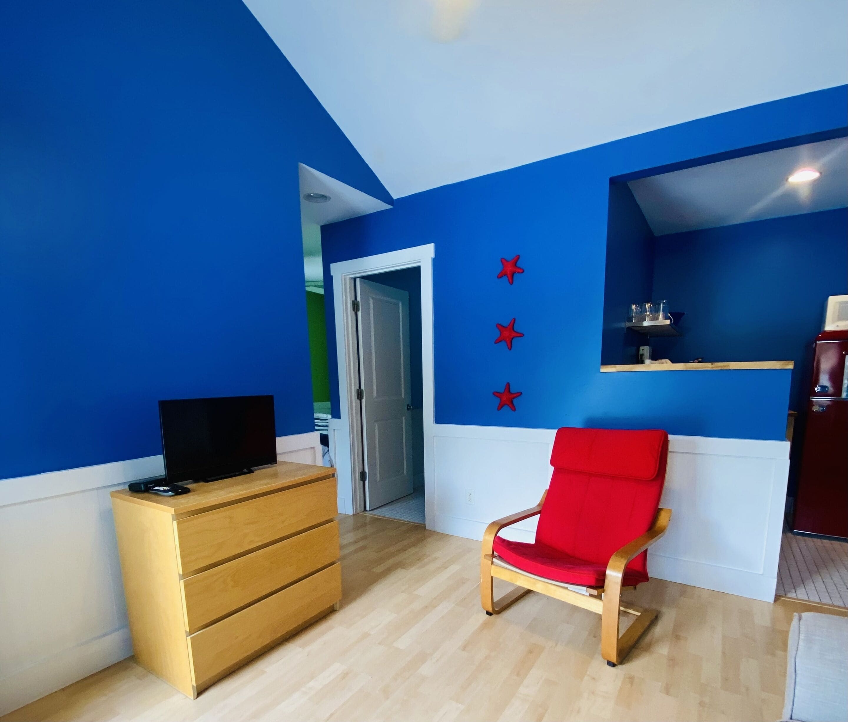A room with blue walls, a wooden dresser, a red chair, and a television on the dresser.