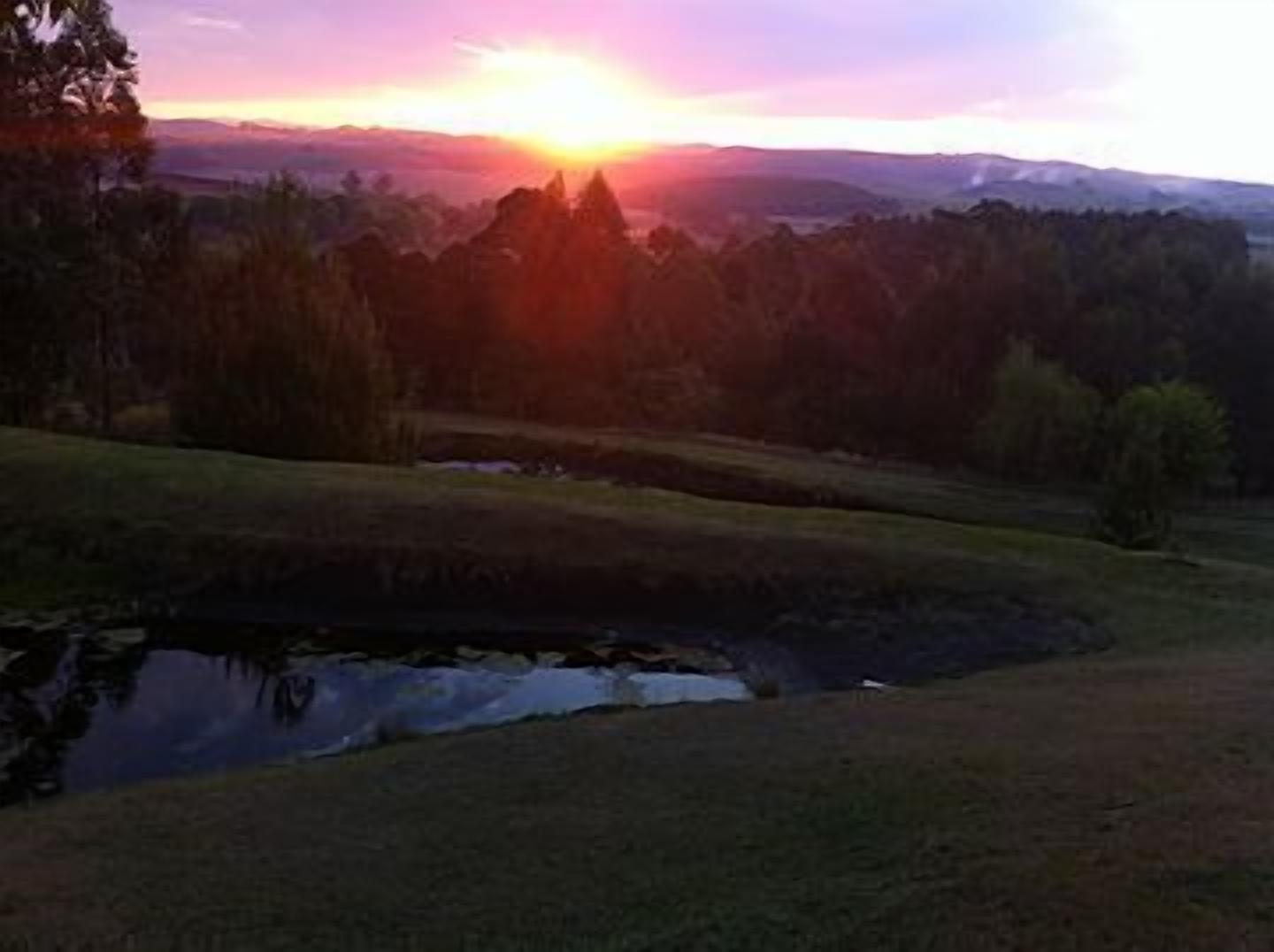 A sunset over a landscape with a body of water, trees, and distant hills.
