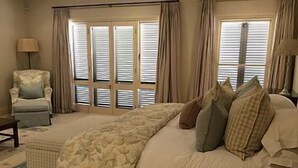 A bedroom with a large bed, a chair, and a nightstand. - Arum Hill Lodge (Balgowan)