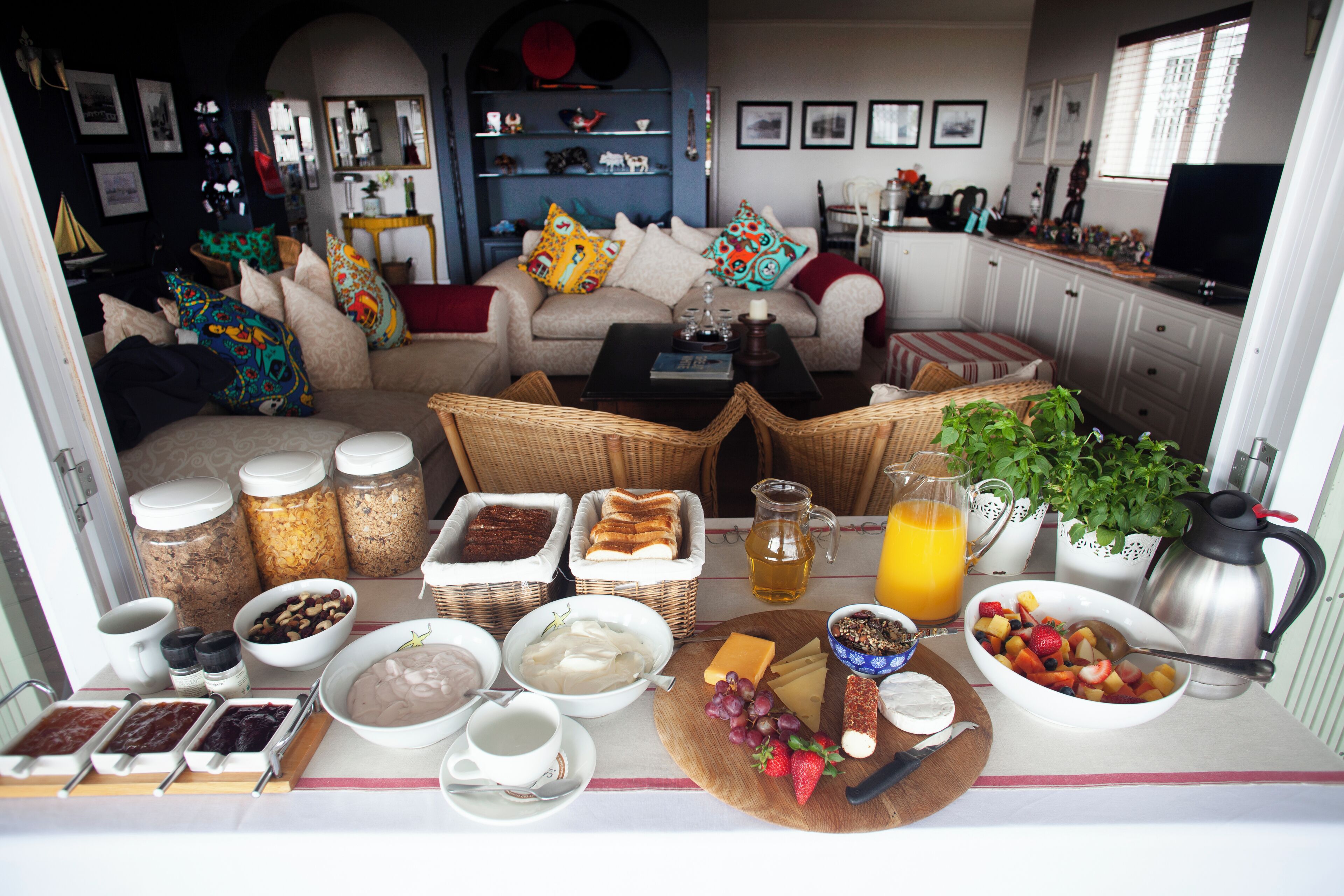 A breakfast setup with various food items, a coffee maker, and a cozy living area with a sofa and cushions.