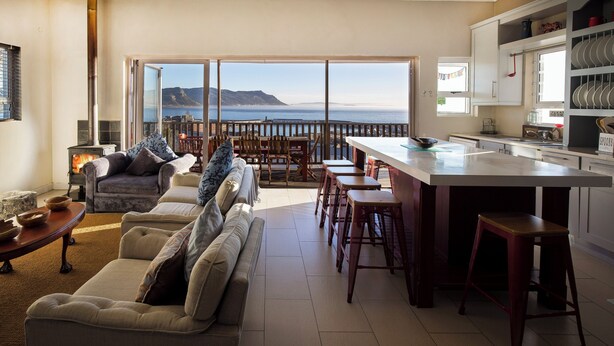 Een woonkamer met een bank, een eethoek met een bar en een keuken met uitzicht op zee.