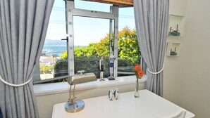 Een kamer met een groot raam, een bureau, een lamp en een vaas met bloemen.