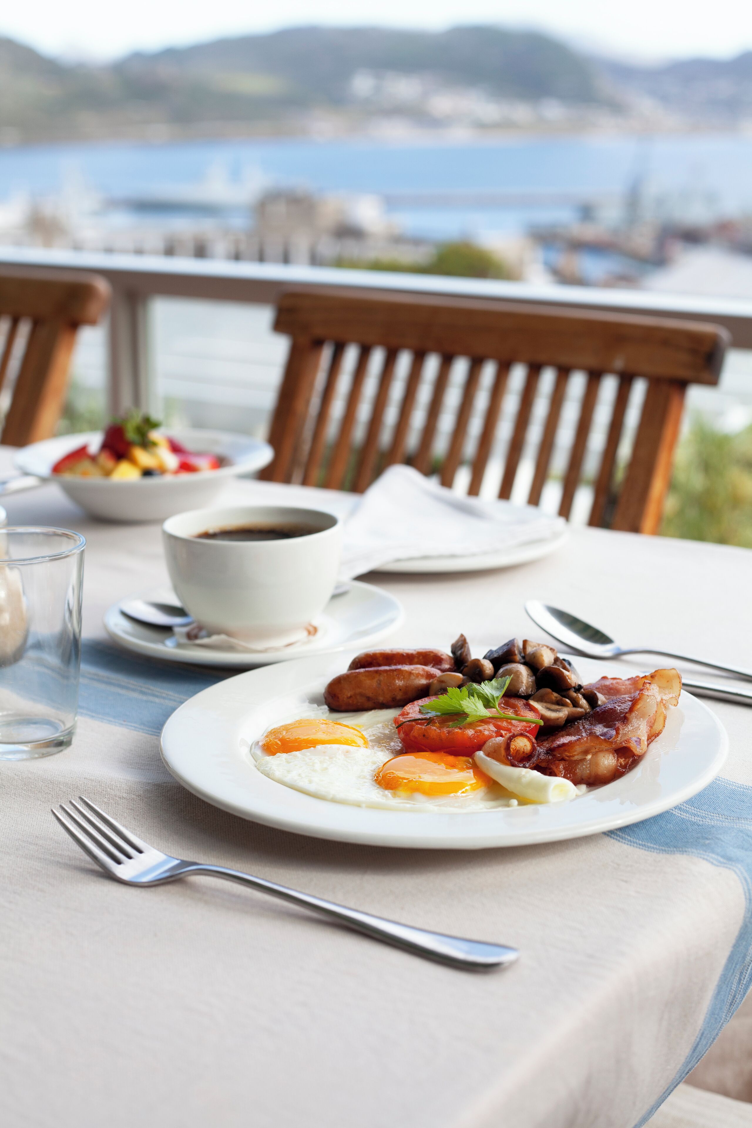 A dining table with breakfast plates, a cup of coffee, and a view of the sea.