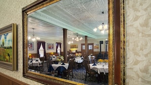 A dining area with tables set for service, a chandelier, and framed artwork on the walls. - The Historic Elk Mountain Hotel (Elk Mountain)