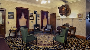 A room with a fireplace, leather chairs, a round rug, and a mounted animal head on the wall. - The Historic Elk Mountain Hotel (Elk Mountain)
