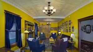 A room with yellow walls, a chandelier, blue upholstered chairs, a wooden floor, and a patterned rug. - The Historic Elk Mountain Hotel (Elk Mountain)