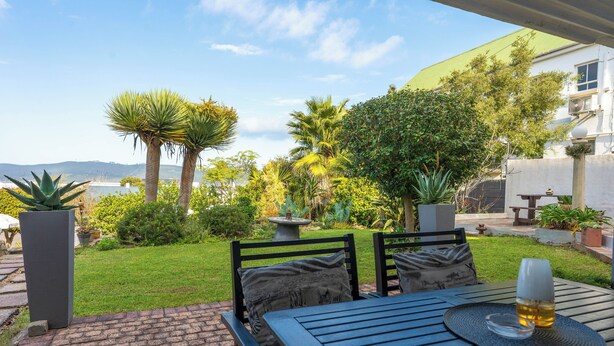 Eine Terrasse im Freien mit Tisch und Stühlen, umgeben von üppiger Vegetation und Blick auf den Ozean.