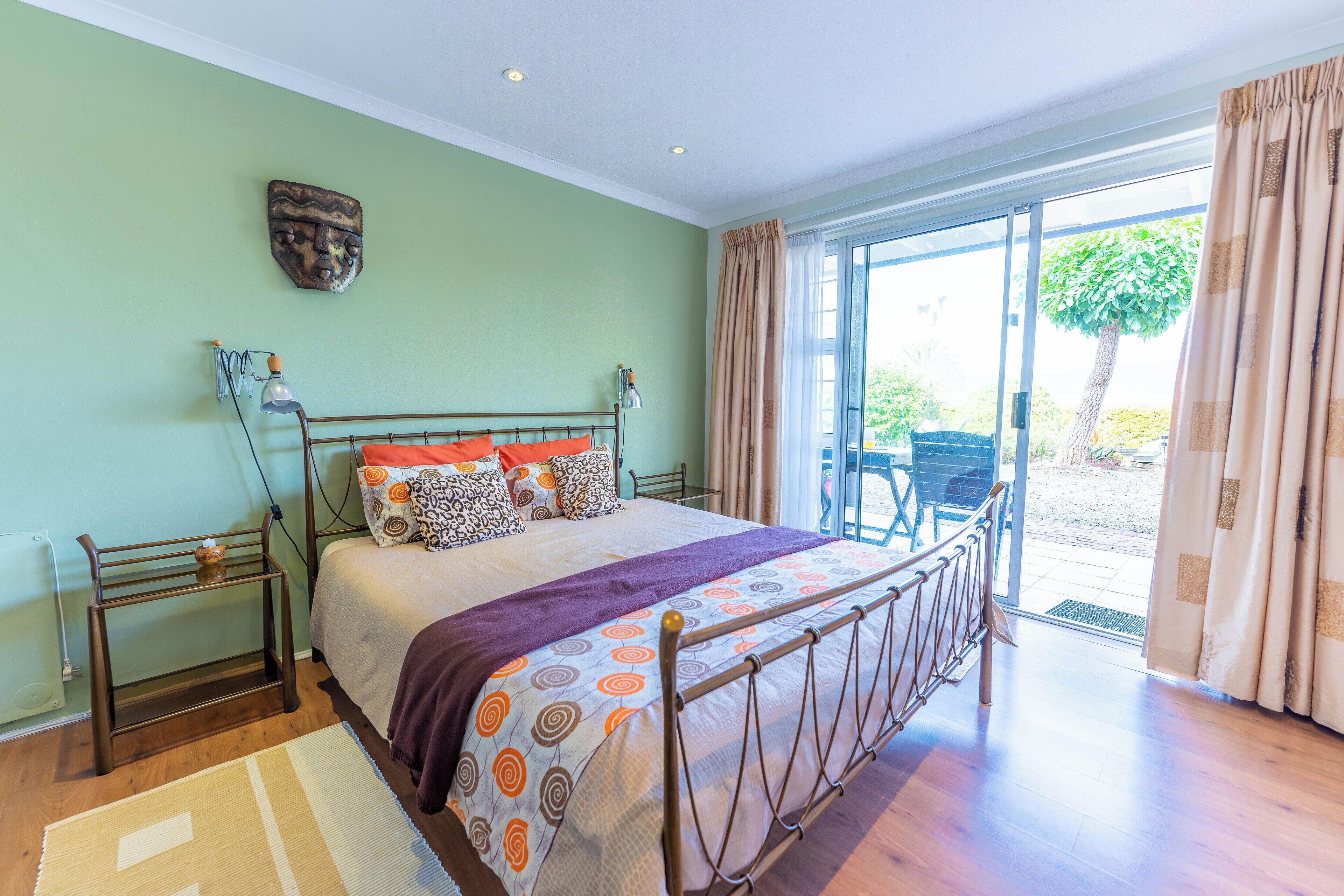 A bedroom with a bed, bedside tables, a nightstand, a window with curtains, and a view of the outdoors.