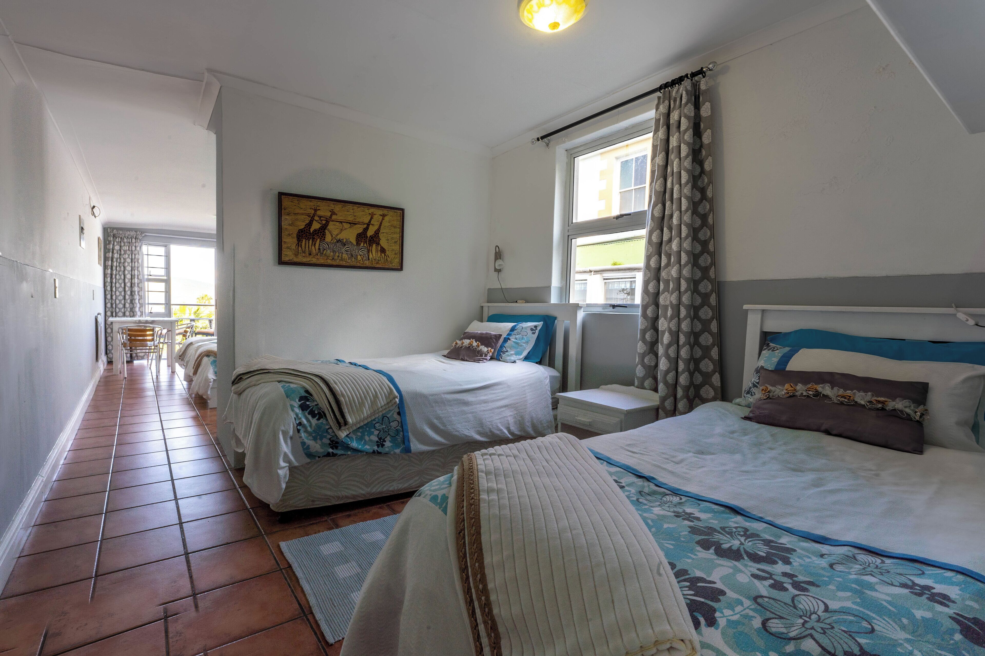 A hotel room with two beds, a small bedside table, a nightstand, and a window with curtains.