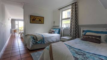 A hotel room with two beds, a small bedside table, a nightstand, and a window with curtains.