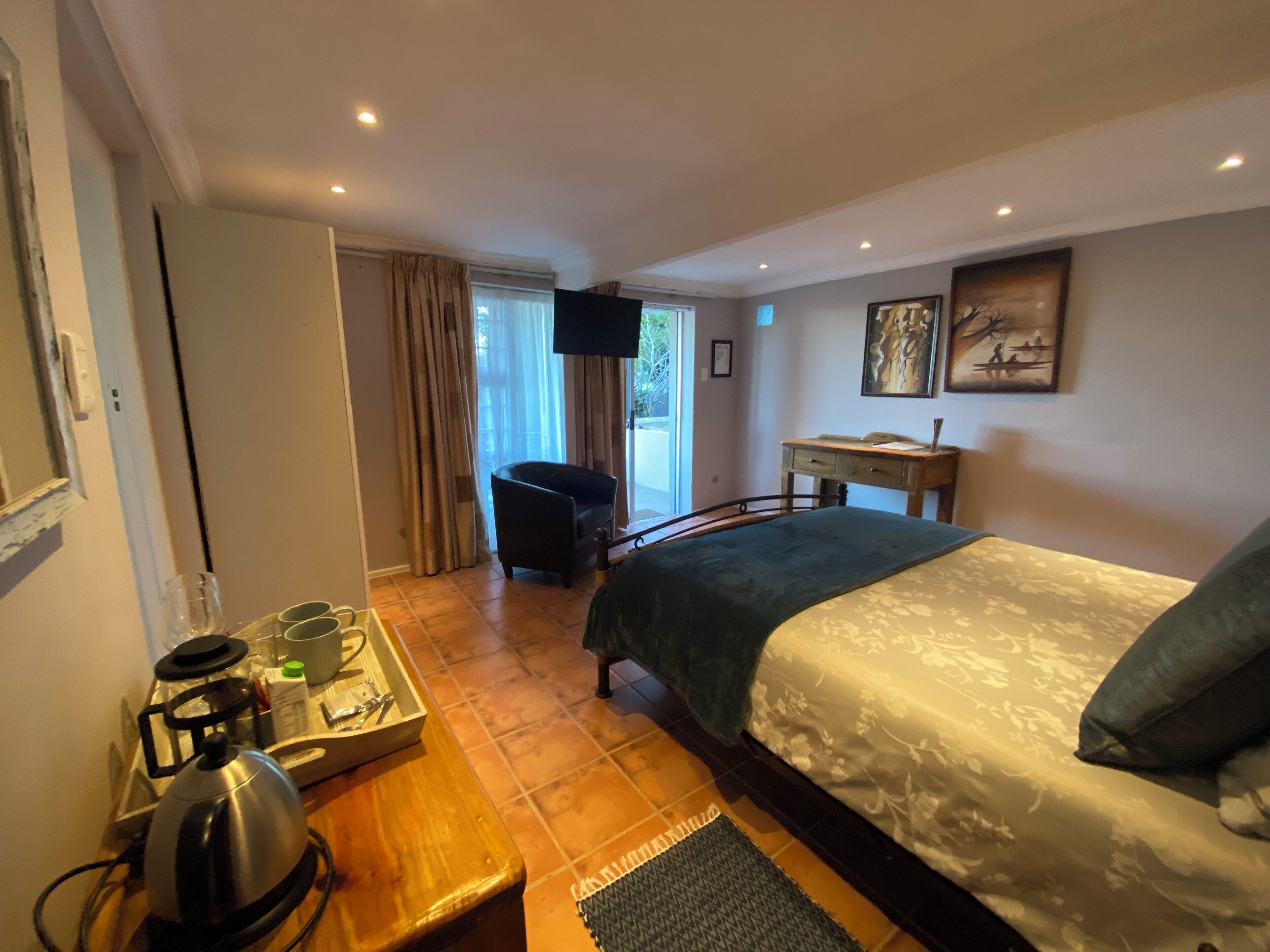A hotel room with a bed, a desk, a chair, a coffee maker, and a television.