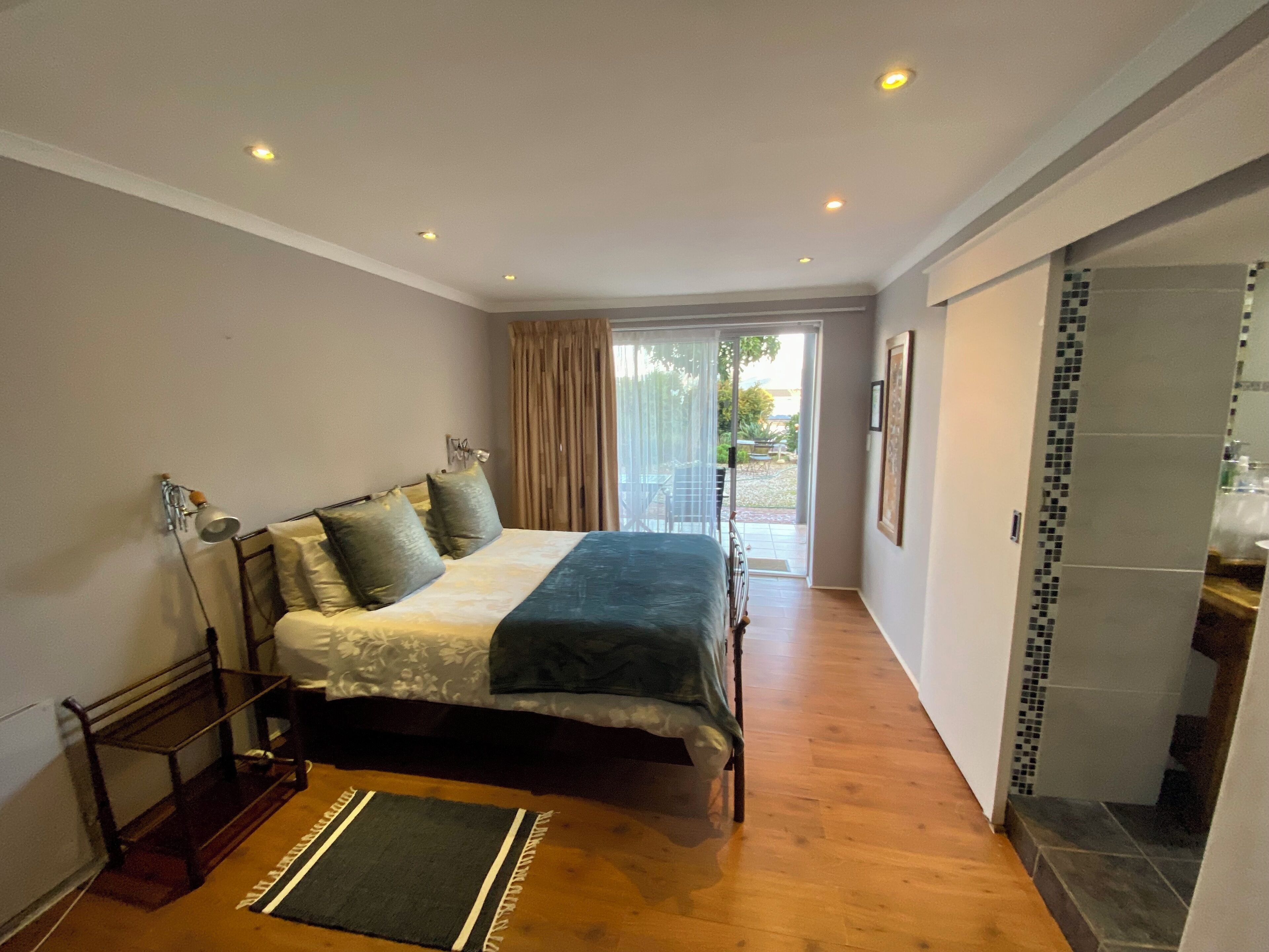 A bedroom with a bed, a bench, a door, and a view of the outside.