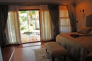 A bedroom with a large bed, a bench, and a view of a garden through a sliding door.