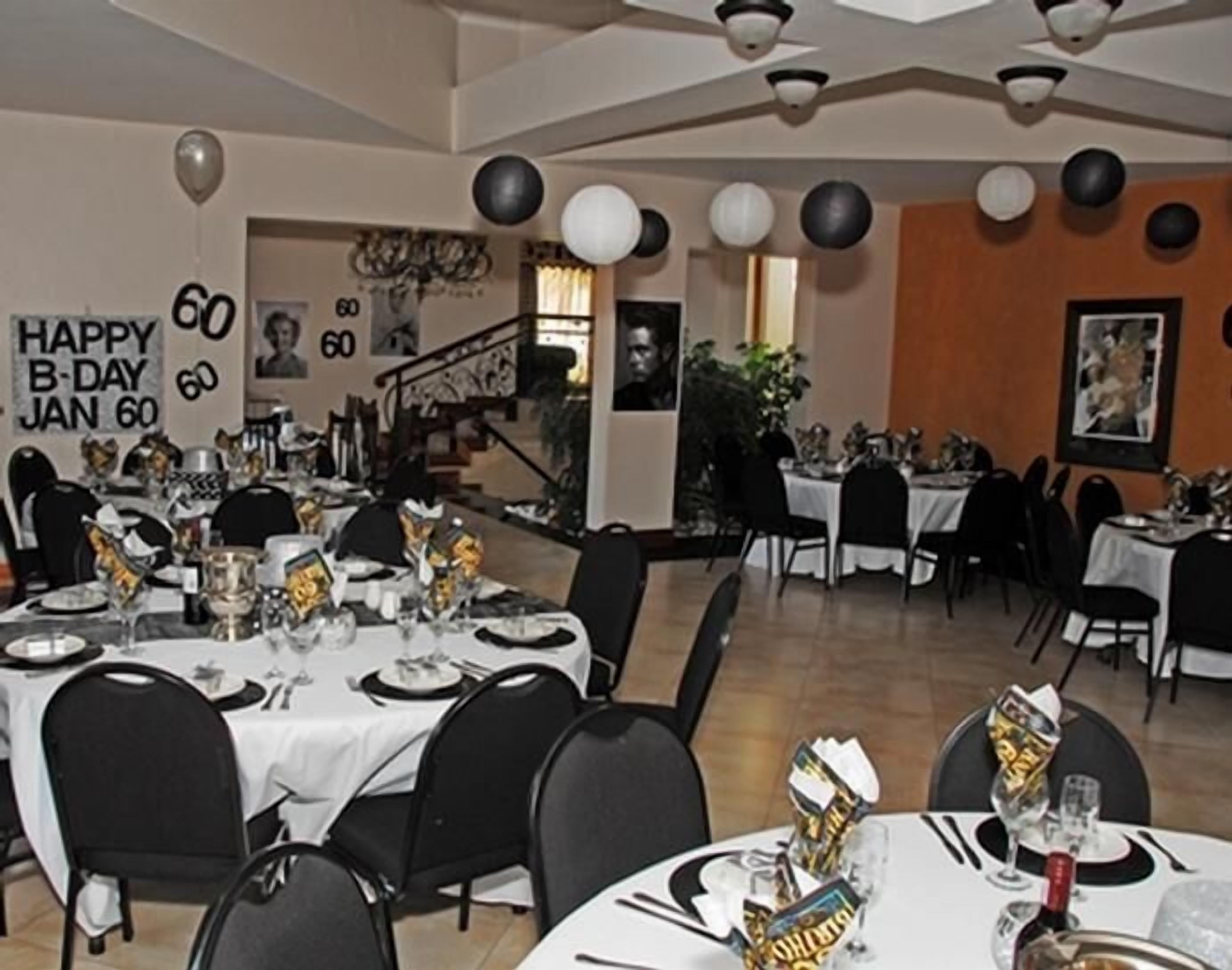 A dining area with tables set for a celebration, balloons, and a 'Happy B-Day Jan 60' sign.