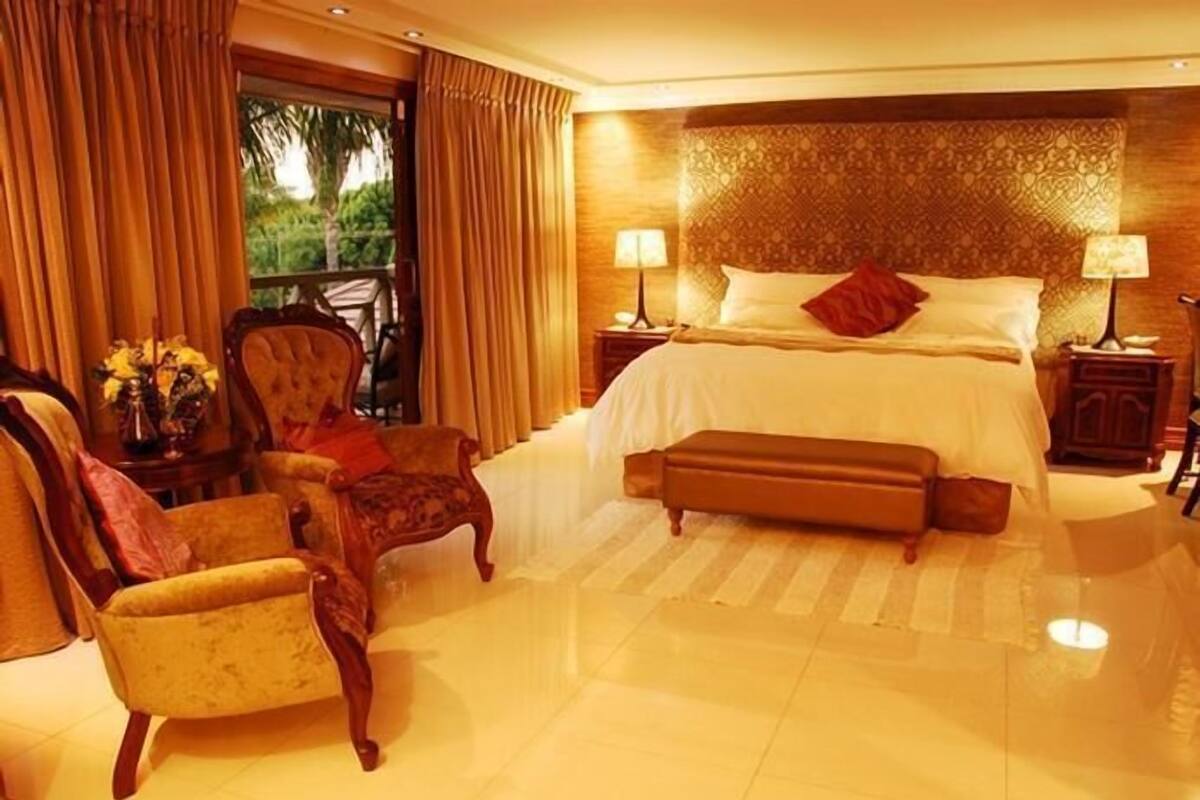 A spacious bedroom with a large bed, two bedside tables, a chair, and a view of greenery outside.
