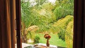 Een kamer met een schuifdeur naar een terras met een tafel en stoelen, omgeven door weelderige beplanting.
