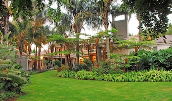 A hotel with a lush garden, palm trees, and a well-maintained lawn.