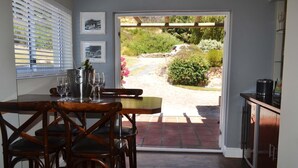 Un coin repas avec une table et des chaises, un réfrigérateur à vin et une vue sur un jardin par une porte ouverte.
