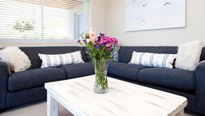 Un salon avec un canapé gris foncé, des coussins blancs et à rayures, une table basse blanche et un vase rempli de fleurs.