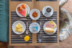 A breakfast setup with plates of scrambled eggs, ham, cheese, and fruit on a striped placemat. - Real Grandeza (Rio de Janeiro)