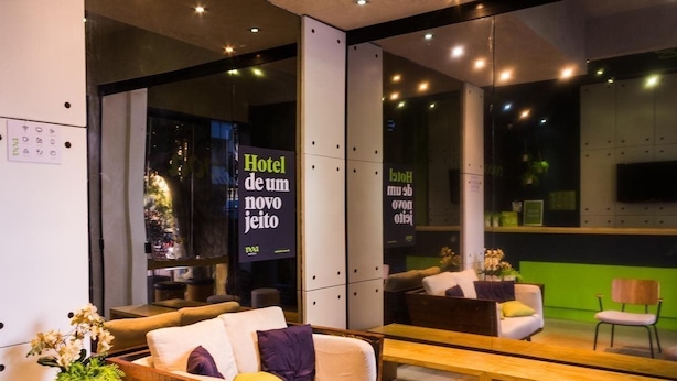 A modern hotel lobby with a sofa, a bench, and a mirror reflecting the space. - Real Grandeza (Rio de Janeiro)