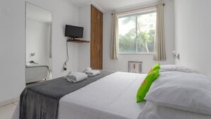 A hotel room with a bed, a television, a mirror, a window with curtains, and a thermostat. - Real Grandeza (Rio de Janeiro)