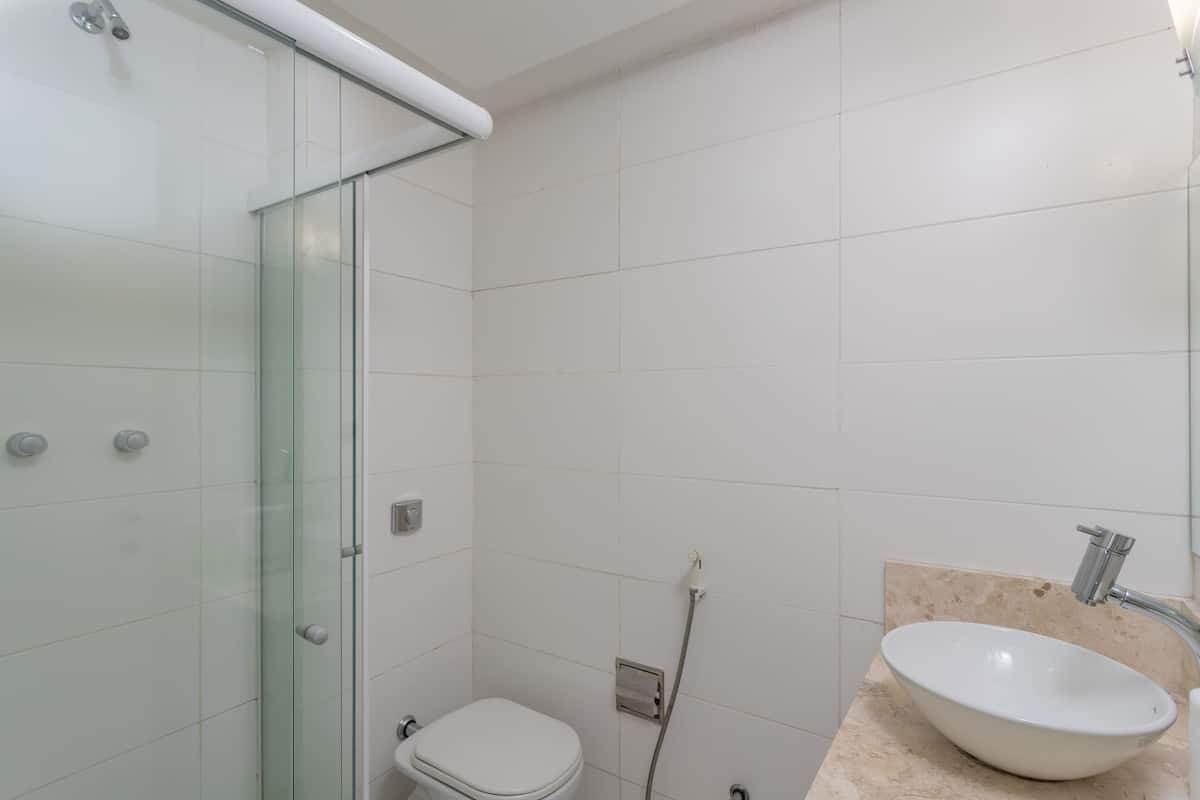 Une salle de bain dotée d’une douche à parois de verre, de toilettes blanches et d’un lavabo avec un plan de toilette de couleur beige.
