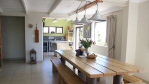 Eine geräumige Küche mit Holztisch und Bänken, einer Pendelleuchte und Blick ins Freie durch ein Fenster.