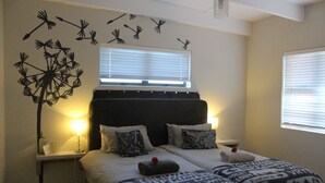 Ein Doppelbett mit gemusterten Bettbezügen, ein Nachttisch mit Lampe und eine Wanddekoration mit Löwenzähnen.